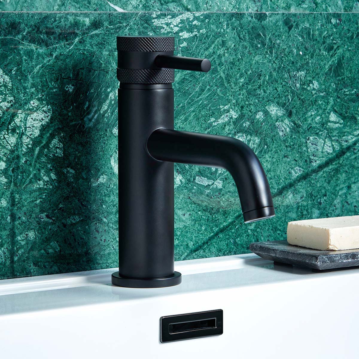 Matt black tap on a basin, backed by green wall tiles