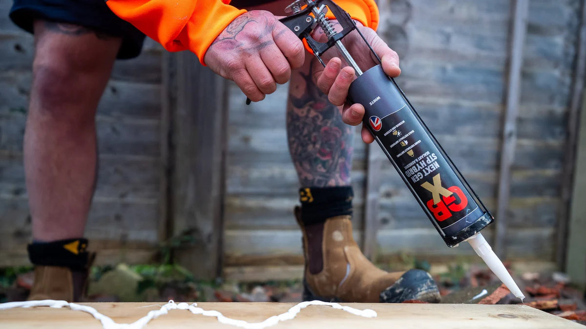 Person applying caulk to a wooden surface with a caulking gun.