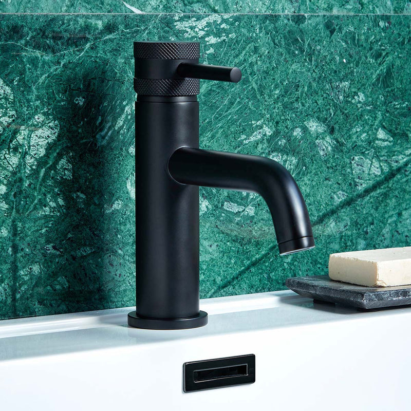 Black faucet on a bathroom sink with a green marble wall in the background