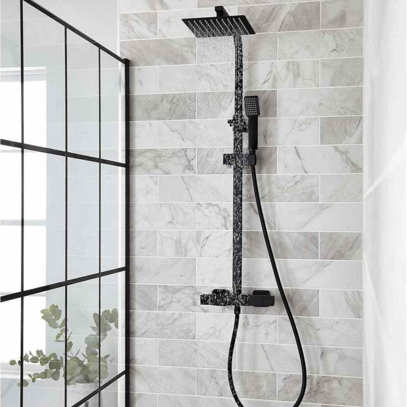 Black shower head and hose on a tiled wall with a glass partition.