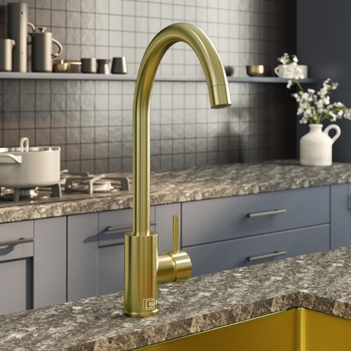 brushed brass kitchen mixer tap in a modern kitchen setting with gray tiles and granite countertops.