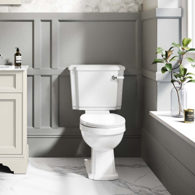 White traditional toilet in a bathroom with gray panelled walls and a sink.